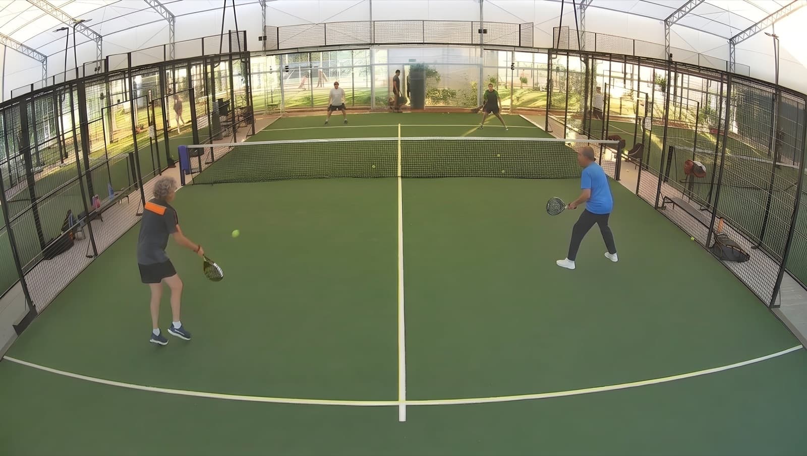 A full padel court with four players, seen from the fixed camera above the back wall